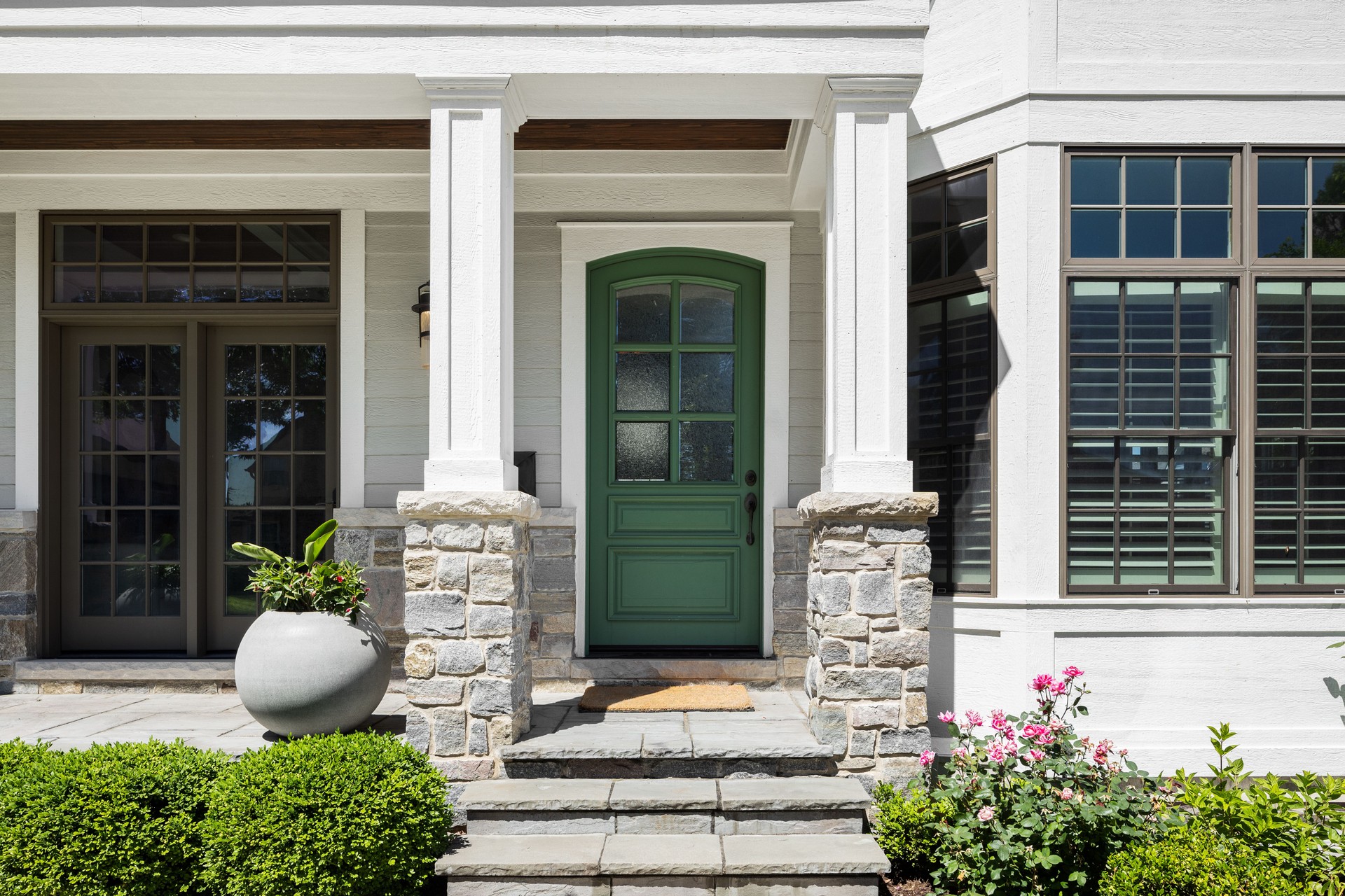 A green front door on a white modern farmhouse with a covered front porch.